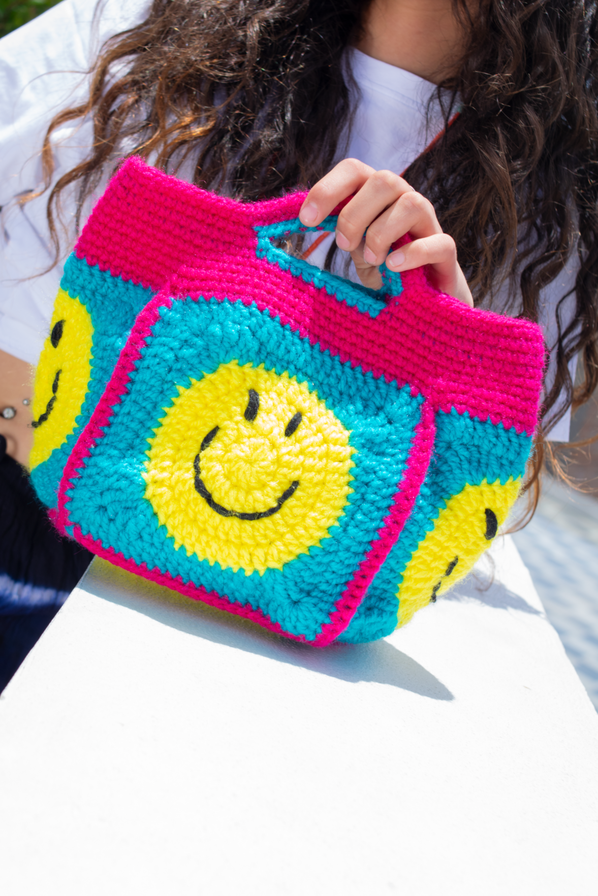 Small rounded bag with yellow smiley patterns.
Turquoise base and integrated pink handles.